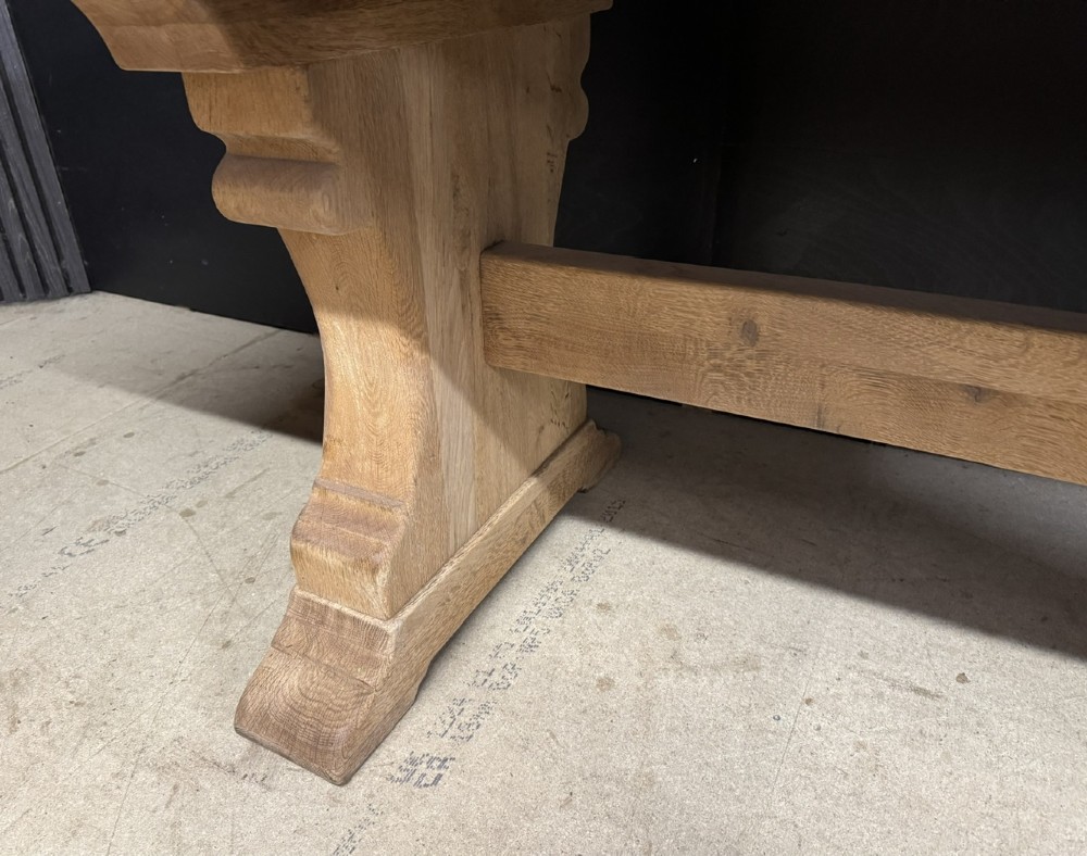 A rectangular bleached oak farmhouse dining table featuring a thick timber top supported by carved trestle legs and a central stretcher. View XI