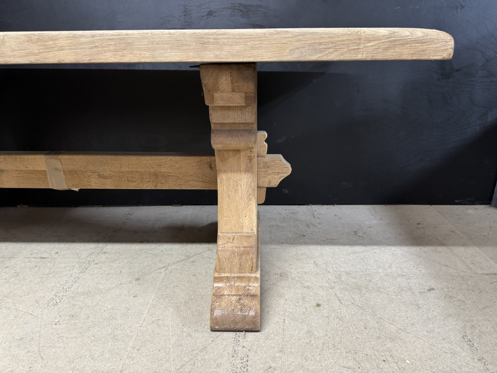 A rectangular bleached oak farmhouse dining table featuring a thick timber top supported by carved trestle legs and a central stretcher. View XIII