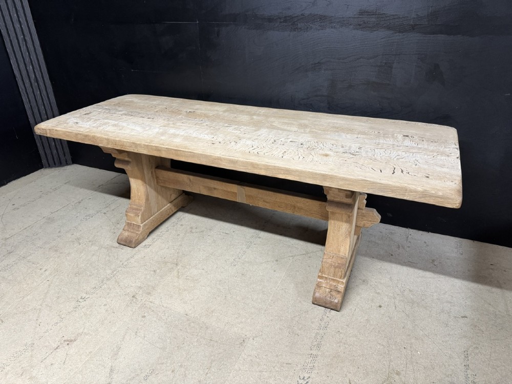 A rectangular bleached oak farmhouse dining table featuring a thick timber top supported by carved trestle legs and a central stretcher. View XIV