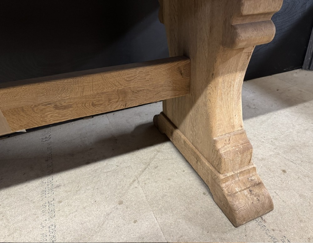 A rectangular bleached oak farmhouse dining table featuring a thick timber top supported by carved trestle legs and a central stretcher. View XV