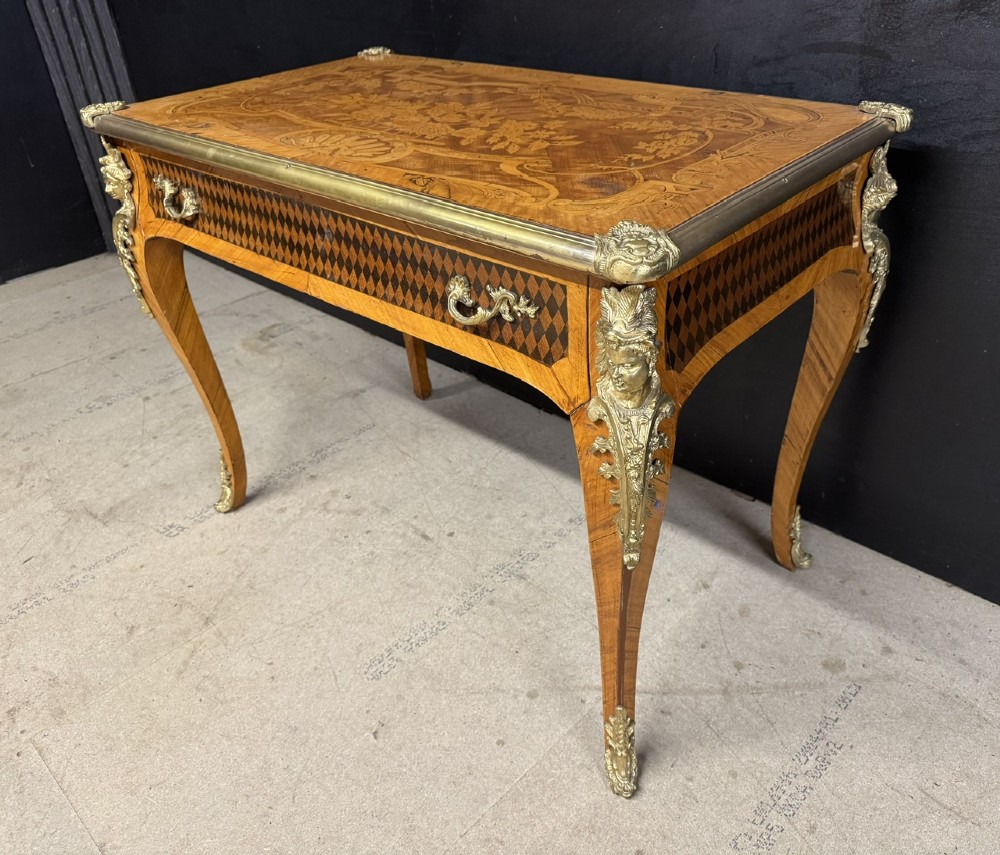 A French Louis XV style marquetry bureau plat featuring floral inlaid wood on the top surface, a diamond parquetry drawer frieze, gilt-bronze corner mounts, and curved cabriole legs. View V