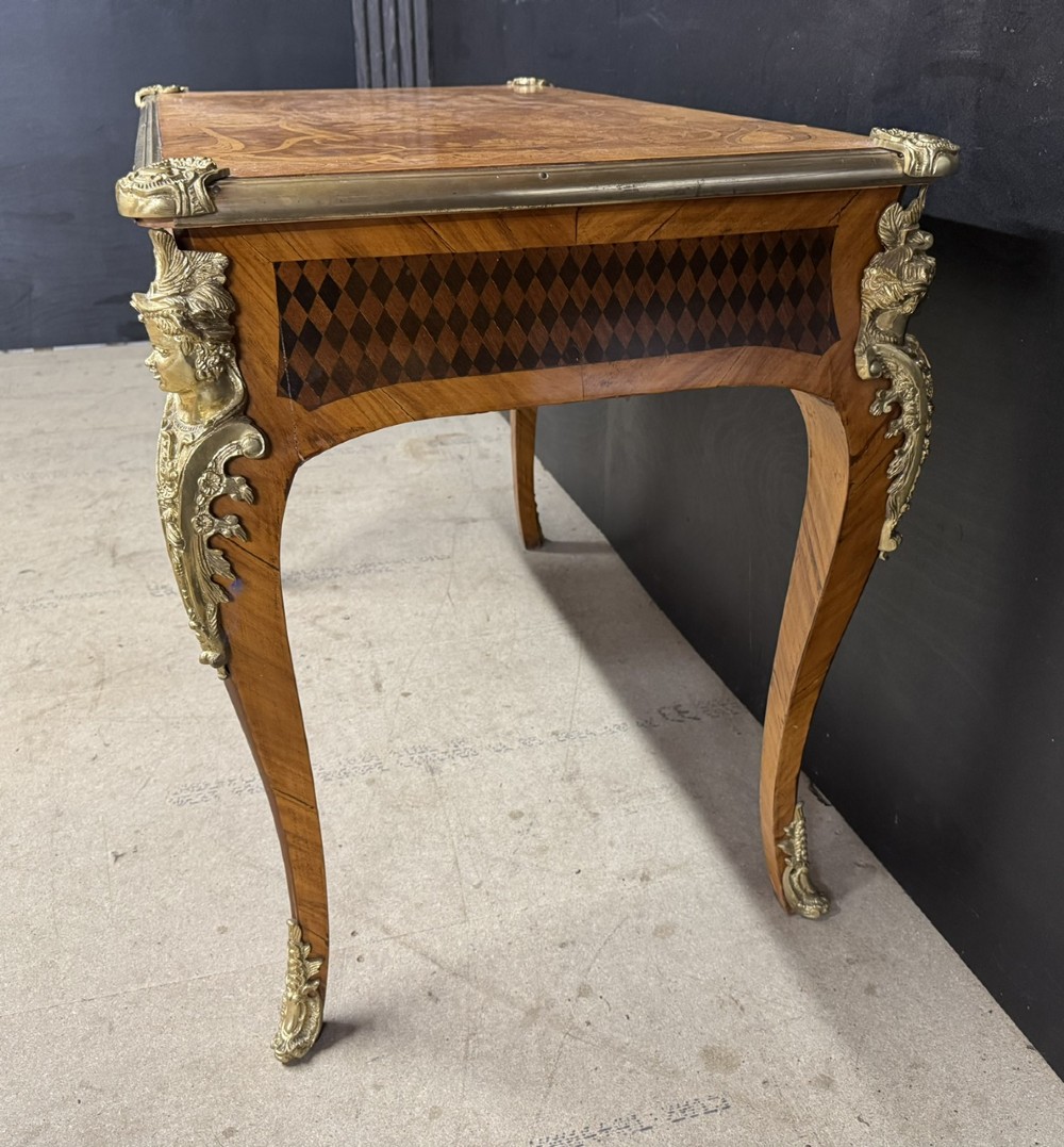 A French Louis XV style marquetry bureau plat featuring floral inlaid wood on the top surface, a diamond parquetry drawer frieze, gilt-bronze corner mounts, and curved cabriole legs. View X