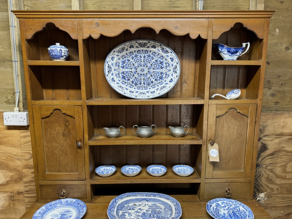A two-part antique pine Welsh dresser featuring an open plate rack flanked by small side cupboards above three frieze drawers and an open pot board base. View II