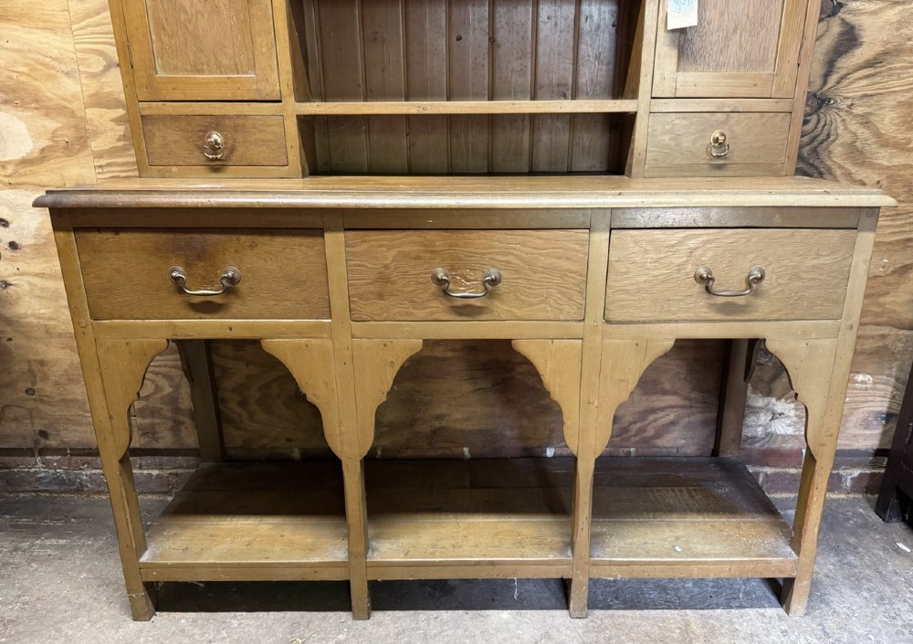 A two-part antique pine Welsh dresser featuring an open plate rack flanked by small side cupboards above three frieze drawers and an open pot board base. View VI