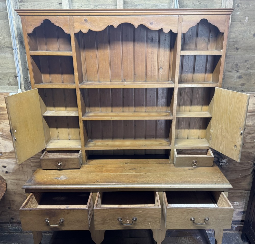 A two-part antique pine Welsh dresser featuring an open plate rack flanked by small side cupboards above three frieze drawers and an open pot board base. View VII