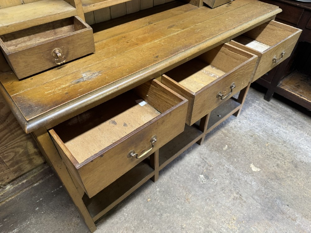 A two-part antique pine Welsh dresser featuring an open plate rack flanked by small side cupboards above three frieze drawers and an open pot board base. View IX