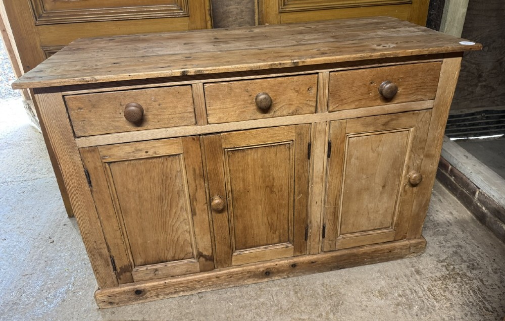 An antique country pine low cupboard featuring three top drawers over three panelled cupboard doors with turned wooden handles. View II