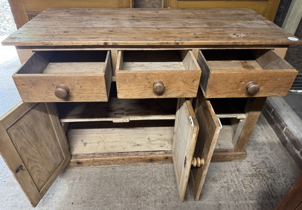 An antique country pine low cupboard featuring three top drawers over three panelled cupboard doors with turned wooden handles. View VI