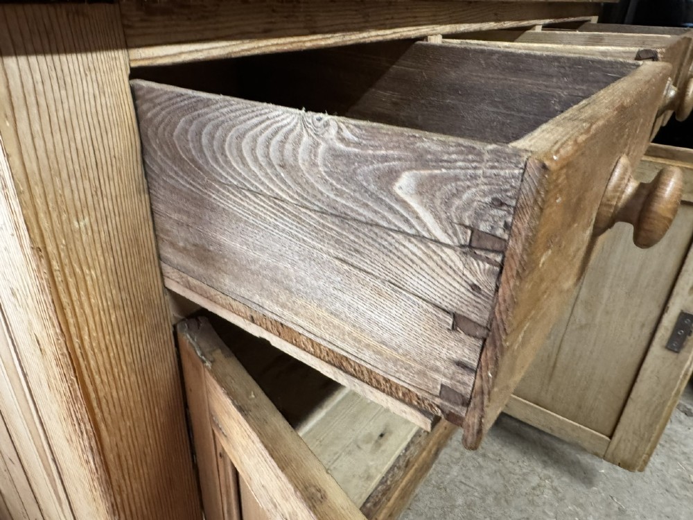 An antique country pine low cupboard featuring three top drawers over three panelled cupboard doors with turned wooden handles. View IX