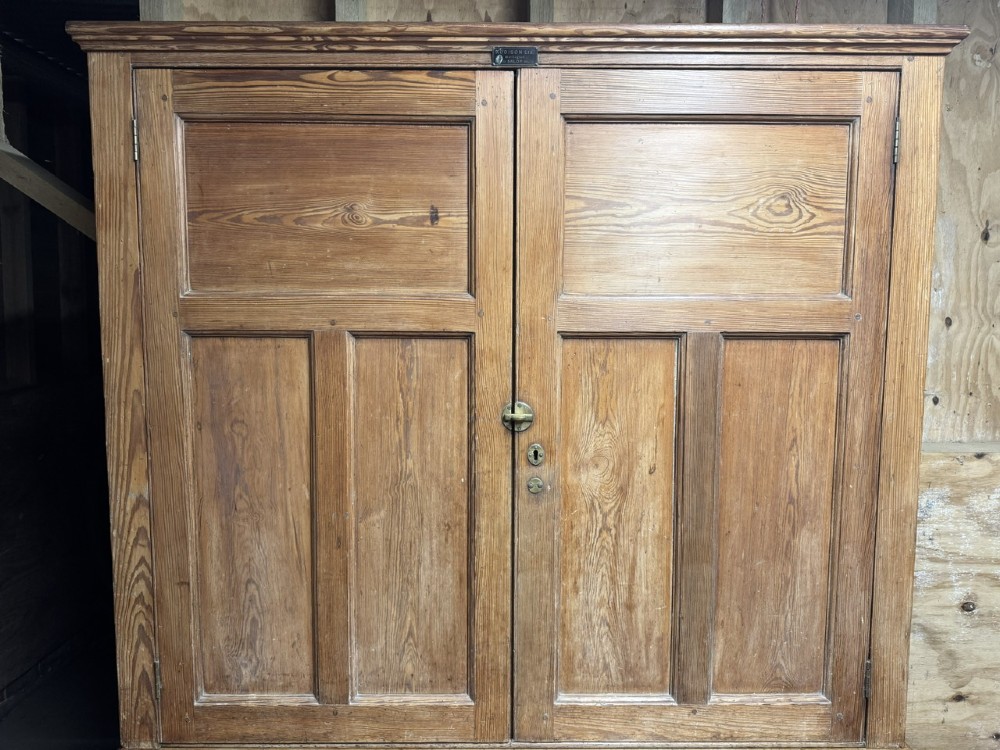 A two-tier nineteenth-century pine school cabinet featuring panelled double doors, brass catches, and a natural waxed finish. View II