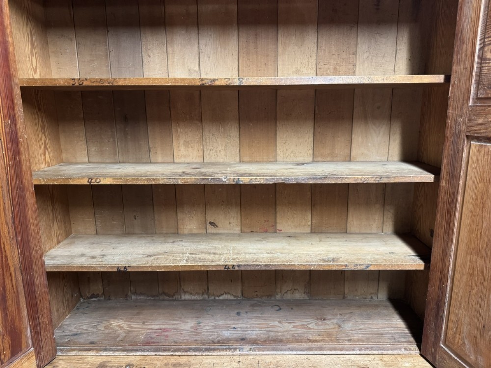 A two-tier nineteenth-century pine school cabinet featuring panelled double doors, brass catches, and a natural waxed finish. View V