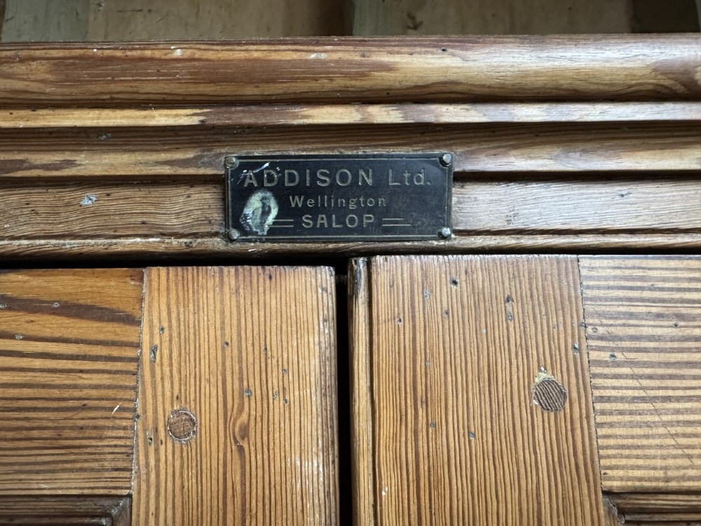A two-tier nineteenth-century pine school cabinet featuring panelled double doors, brass catches, and a natural waxed finish. View IX