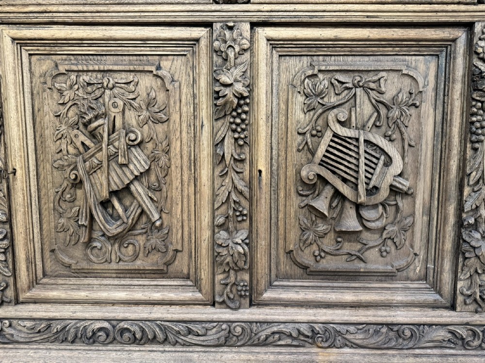 A three-door carved light oak sideboard featuring detailed relief panels depicting artistic and musical instruments. View IV