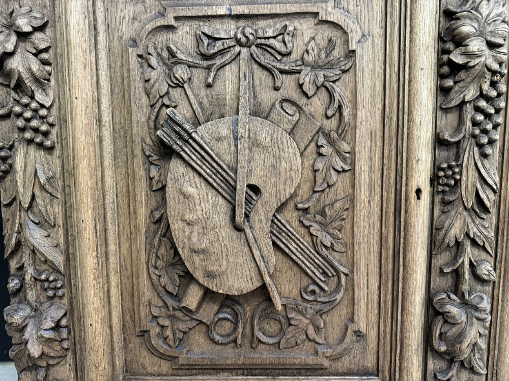 A three-door carved light oak sideboard featuring detailed relief panels depicting artistic and musical instruments. View V