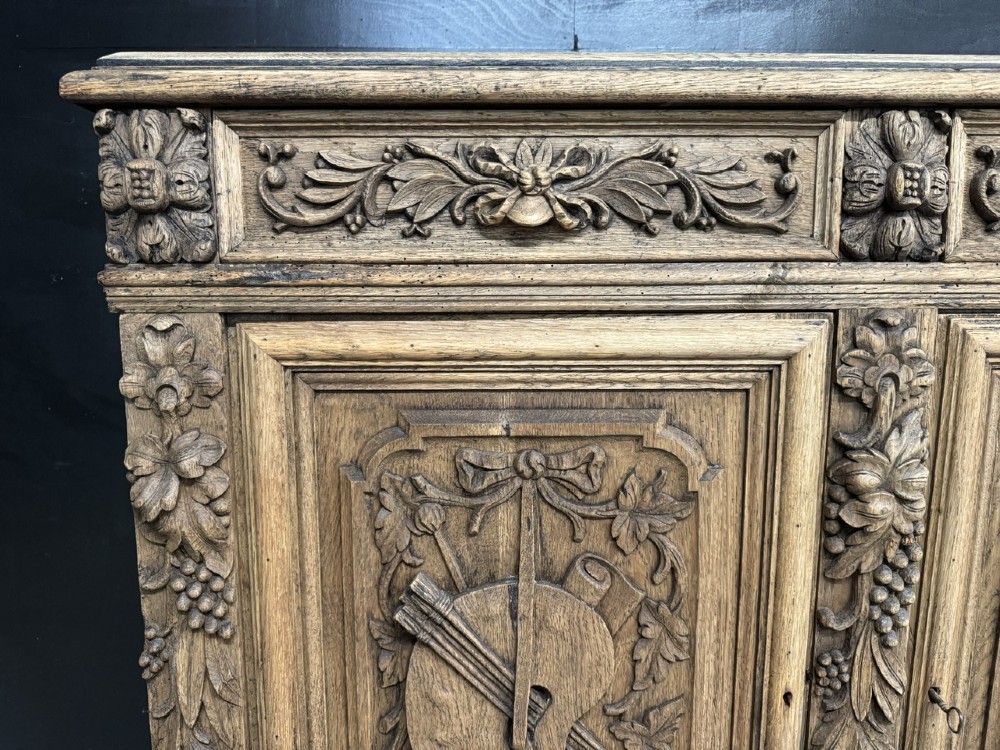 A three-door carved light oak sideboard featuring detailed relief panels depicting artistic and musical instruments. View VI
