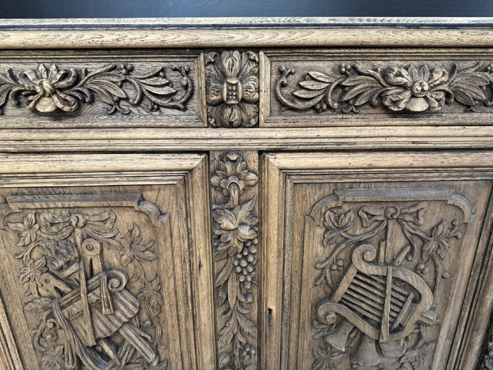 A three-door carved light oak sideboard featuring detailed relief panels depicting artistic and musical instruments. View VII
