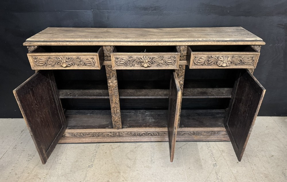A three-door carved light oak sideboard featuring detailed relief panels depicting artistic and musical instruments. View VIII