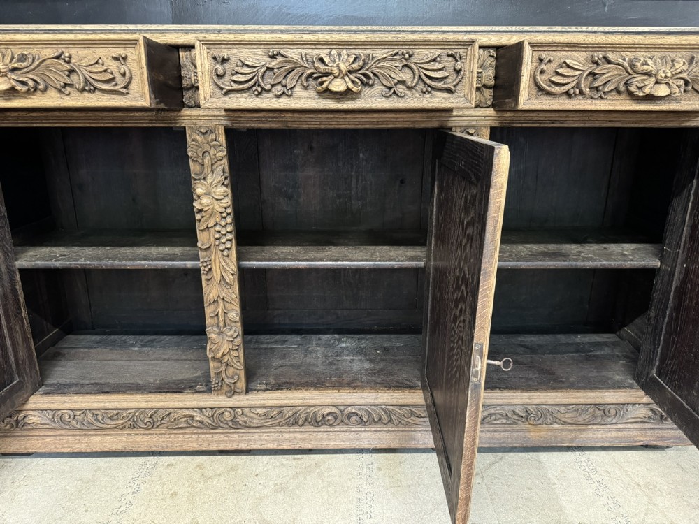 A three-door carved light oak sideboard featuring detailed relief panels depicting artistic and musical instruments. View IX