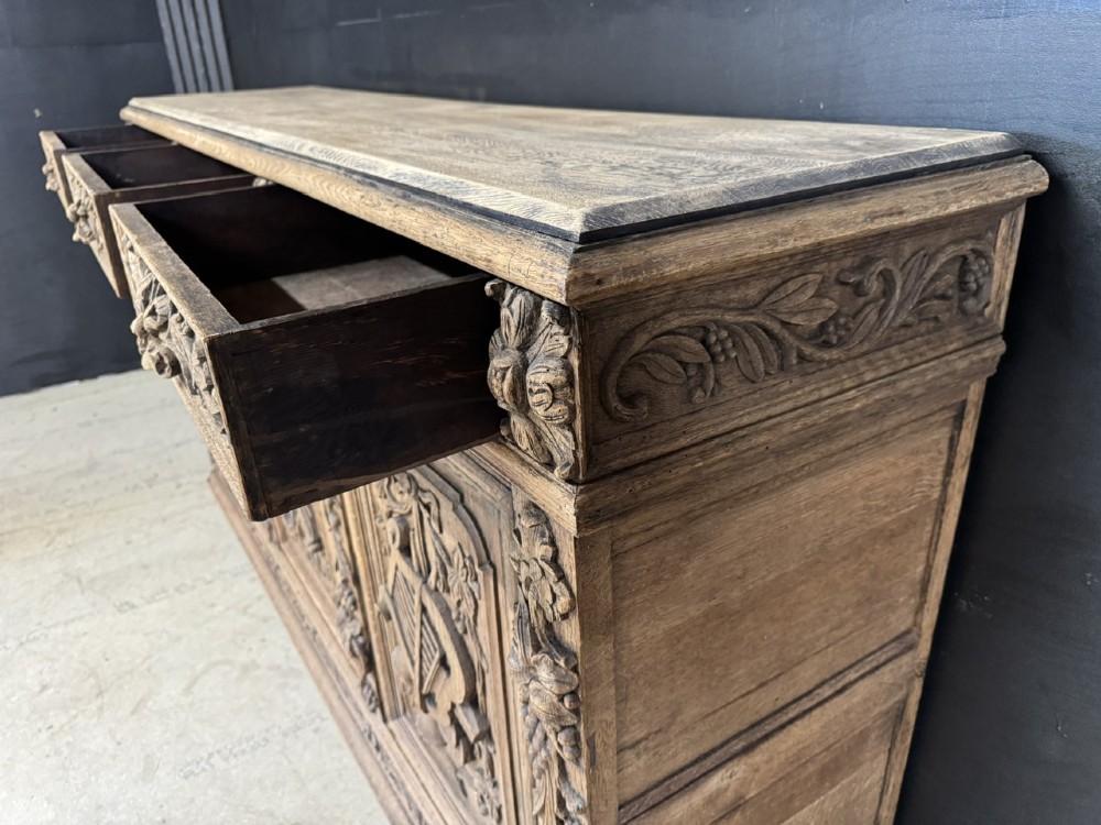 A three-door carved light oak sideboard featuring detailed relief panels depicting artistic and musical instruments. View X