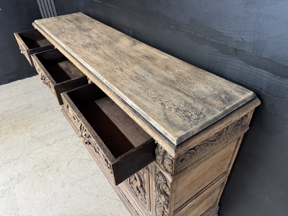 A three-door carved light oak sideboard featuring detailed relief panels depicting artistic and musical instruments. View XI