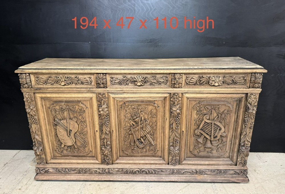 A three-door carved light oak sideboard featuring detailed relief panels depicting artistic and musical instruments. View XV