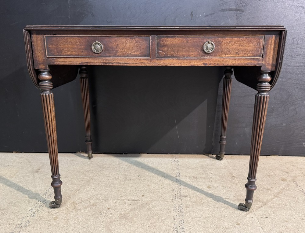 A Georgian style dark mahogany sofa table featuring two drawers with brass ring pulls, drop leaves on either side, and reeded tapered legs on brass castors. View III