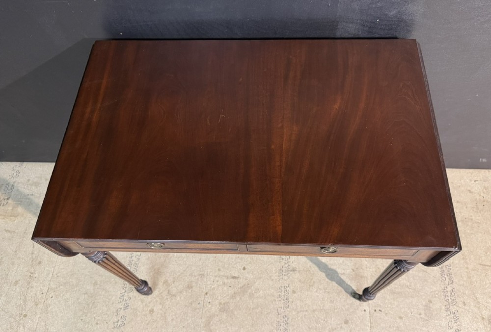 A Georgian style dark mahogany sofa table featuring two drawers with brass ring pulls, drop leaves on either side, and reeded tapered legs on brass castors. View IV