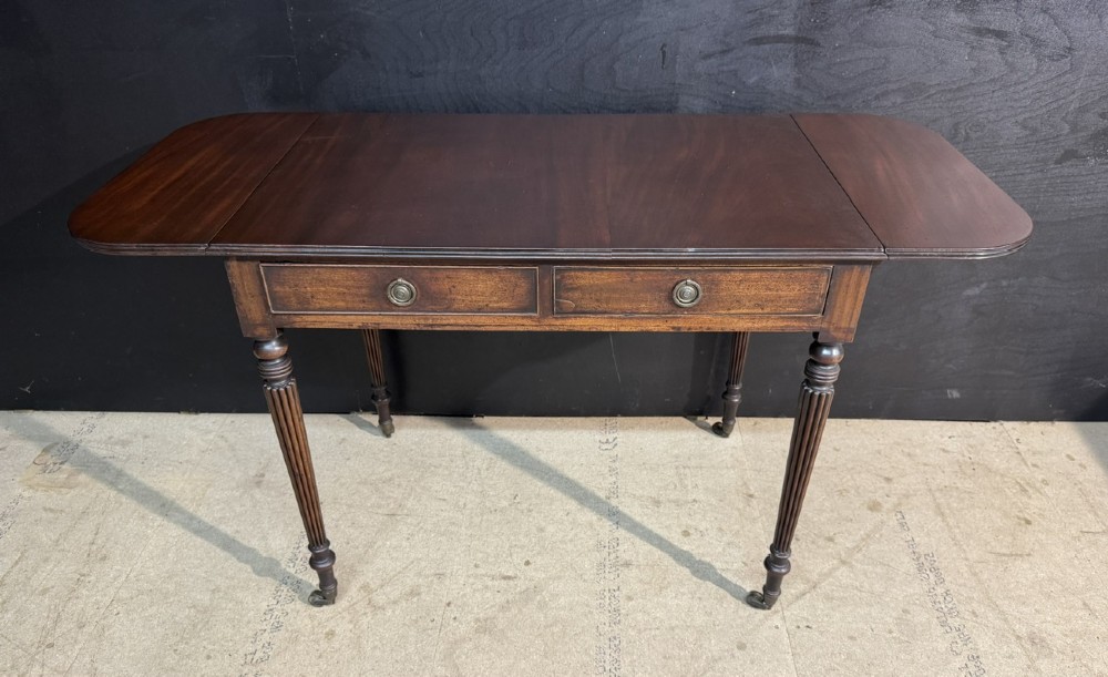 A Georgian style dark mahogany sofa table featuring two drawers with brass ring pulls, drop leaves on either side, and reeded tapered legs on brass castors. View VI