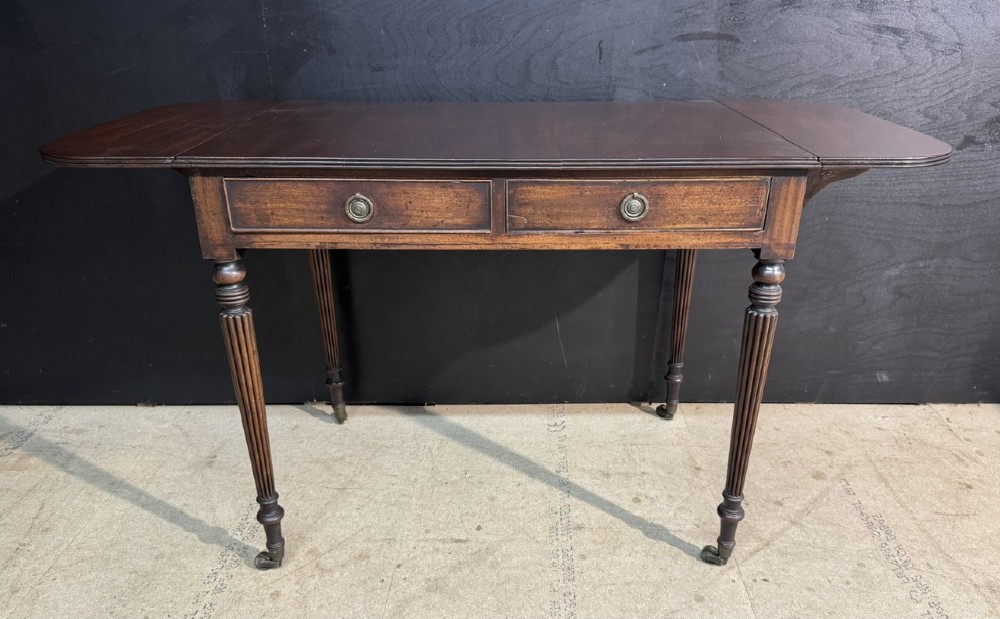 A Georgian style dark mahogany sofa table featuring two drawers with brass ring pulls, drop leaves on either side, and reeded tapered legs on brass castors. View VII