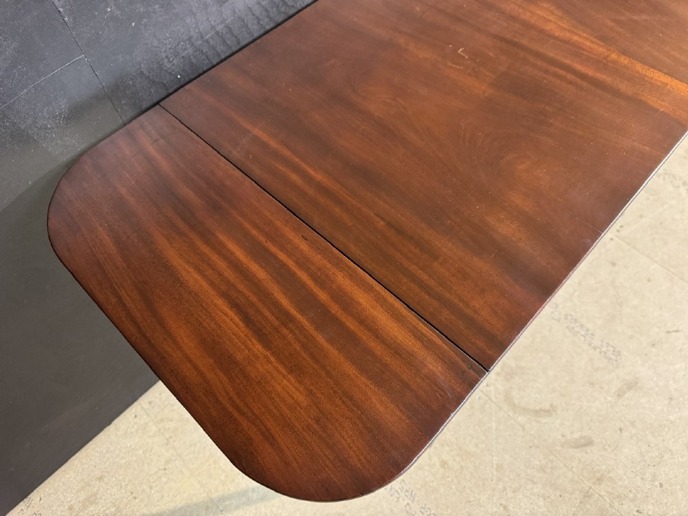 A Georgian style dark mahogany sofa table featuring two drawers with brass ring pulls, drop leaves on either side, and reeded tapered legs on brass castors. View XI