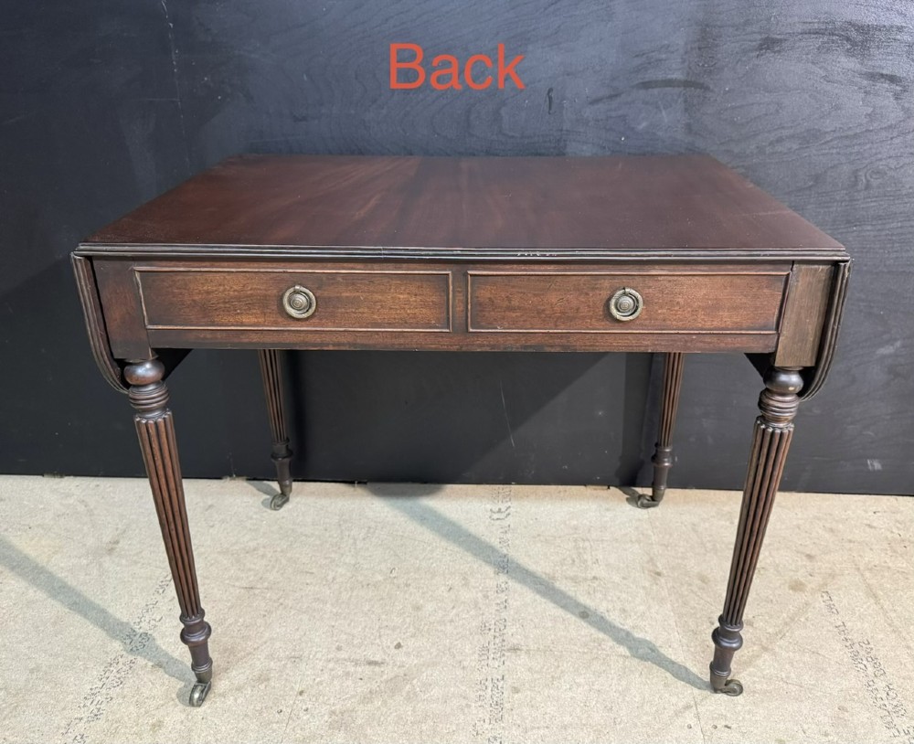 A Georgian style dark mahogany sofa table featuring two drawers with brass ring pulls, drop leaves on either side, and reeded tapered legs on brass castors. View XII