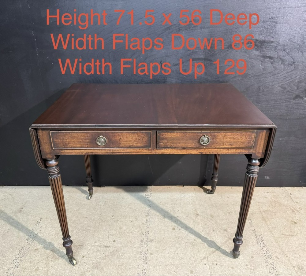 A Georgian style dark mahogany sofa table featuring two drawers with brass ring pulls, drop leaves on either side, and reeded tapered legs on brass castors. View XV