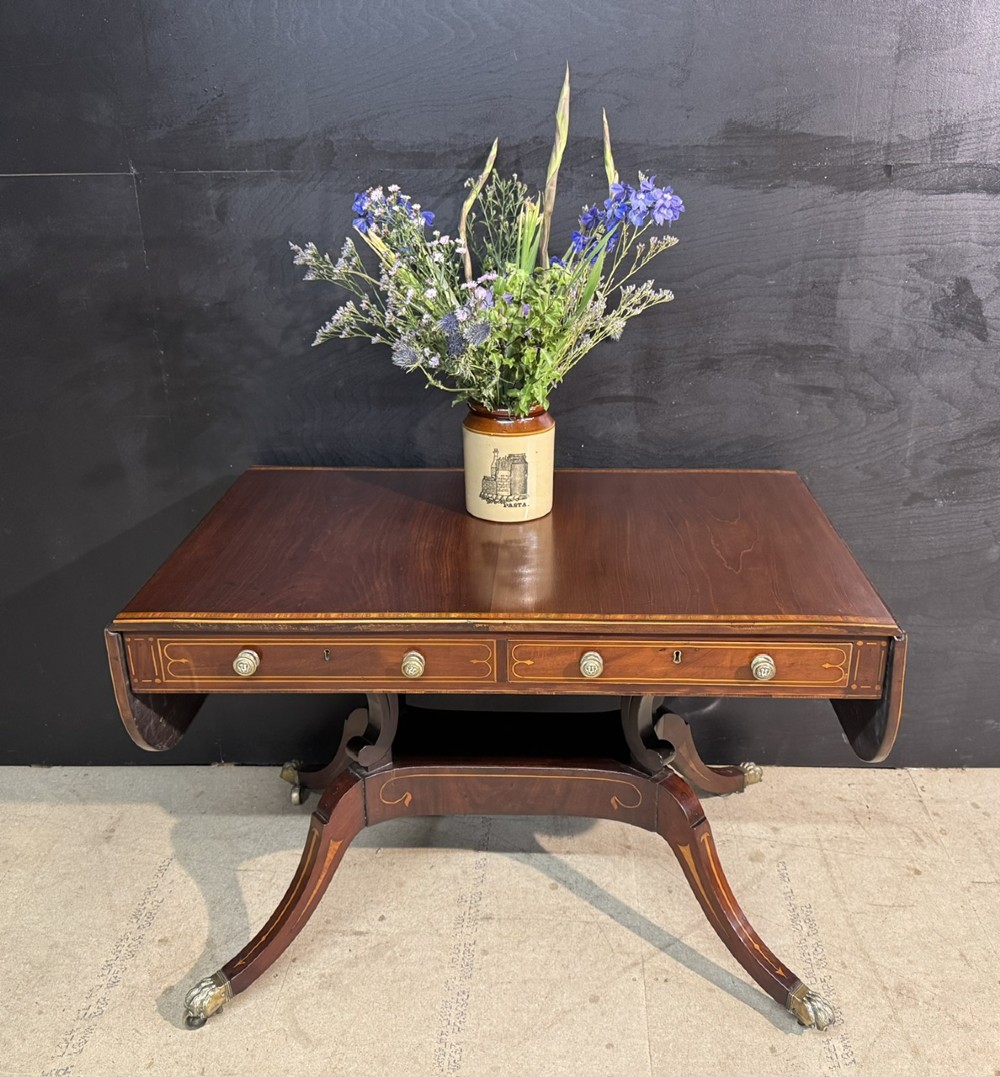 A Georgian mahogany sofa table featuring two inline drawers with satinwood string inlay, drop leaves, twin-pillar supports, and splayed legs ending in brass claw feet on castors. View II
