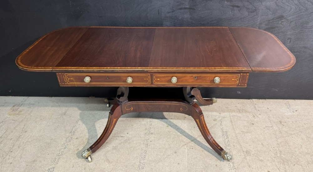 A Georgian mahogany sofa table featuring two inline drawers with satinwood string inlay, drop leaves, twin-pillar supports, and splayed legs ending in brass claw feet on castors. View III
