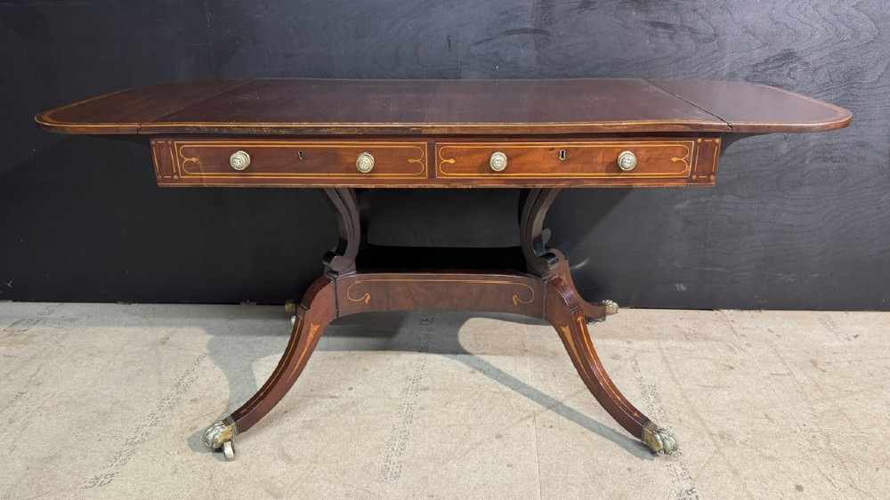 A Georgian mahogany sofa table featuring two inline drawers with satinwood string inlay, drop leaves, twin-pillar supports, and splayed legs ending in brass claw feet on castors. View IV