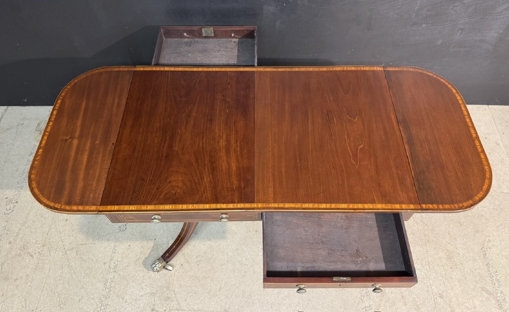 A Georgian mahogany sofa table featuring two inline drawers with satinwood string inlay, drop leaves, twin-pillar supports, and splayed legs ending in brass claw feet on castors. View IX