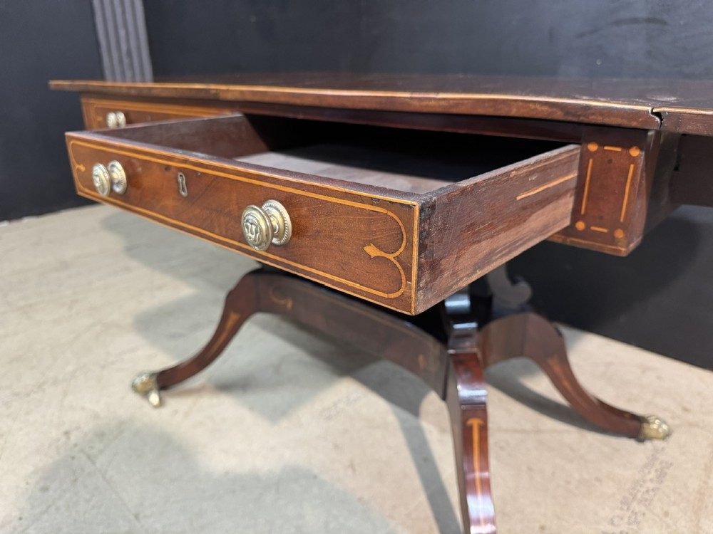 A Georgian mahogany sofa table featuring two inline drawers with satinwood string inlay, drop leaves, twin-pillar supports, and splayed legs ending in brass claw feet on castors. View XI