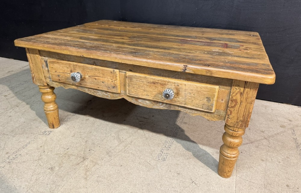 A rectangular rustic pine coffee table featuring a plank top, two front drawers with decorative ceramic knobs, and four turned wooden legs.