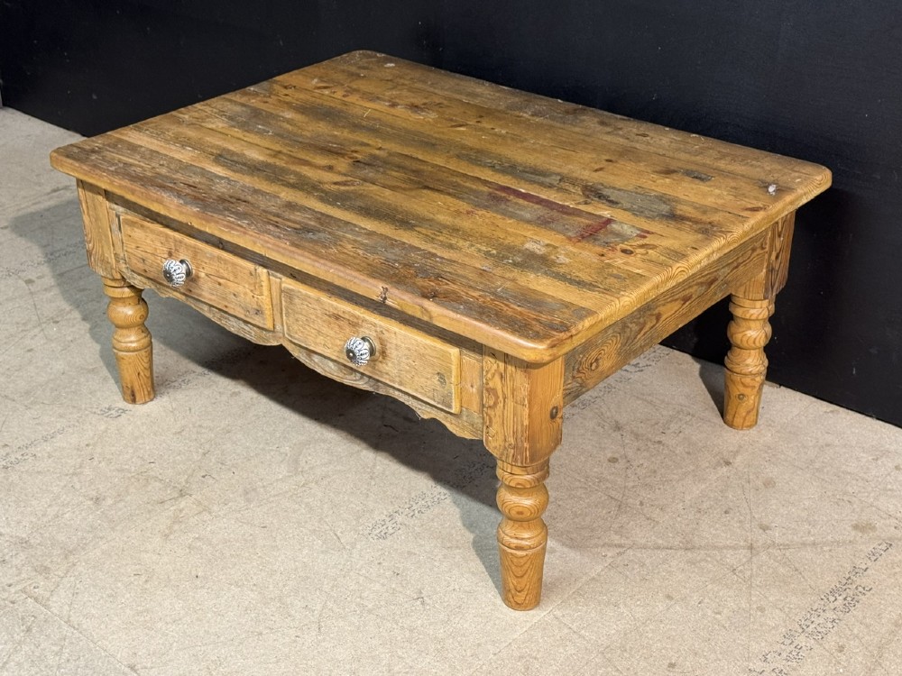 A rectangular rustic pine coffee table featuring a plank top, two front drawers with decorative ceramic knobs, and four turned wooden legs. View V