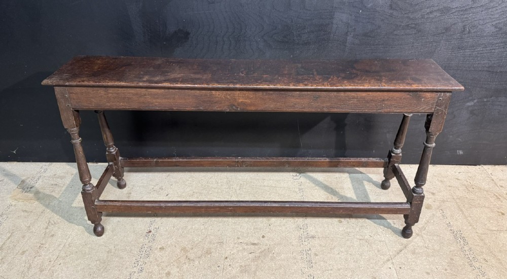 A long dark oak Georgian joint stool with turned legs, a rectangular top, and lower wooden stretchers.
