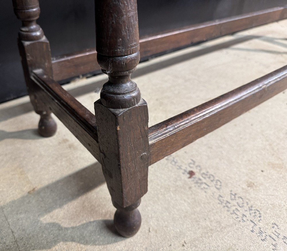 A long dark oak Georgian joint stool with turned legs, a rectangular top, and lower wooden stretchers. View X