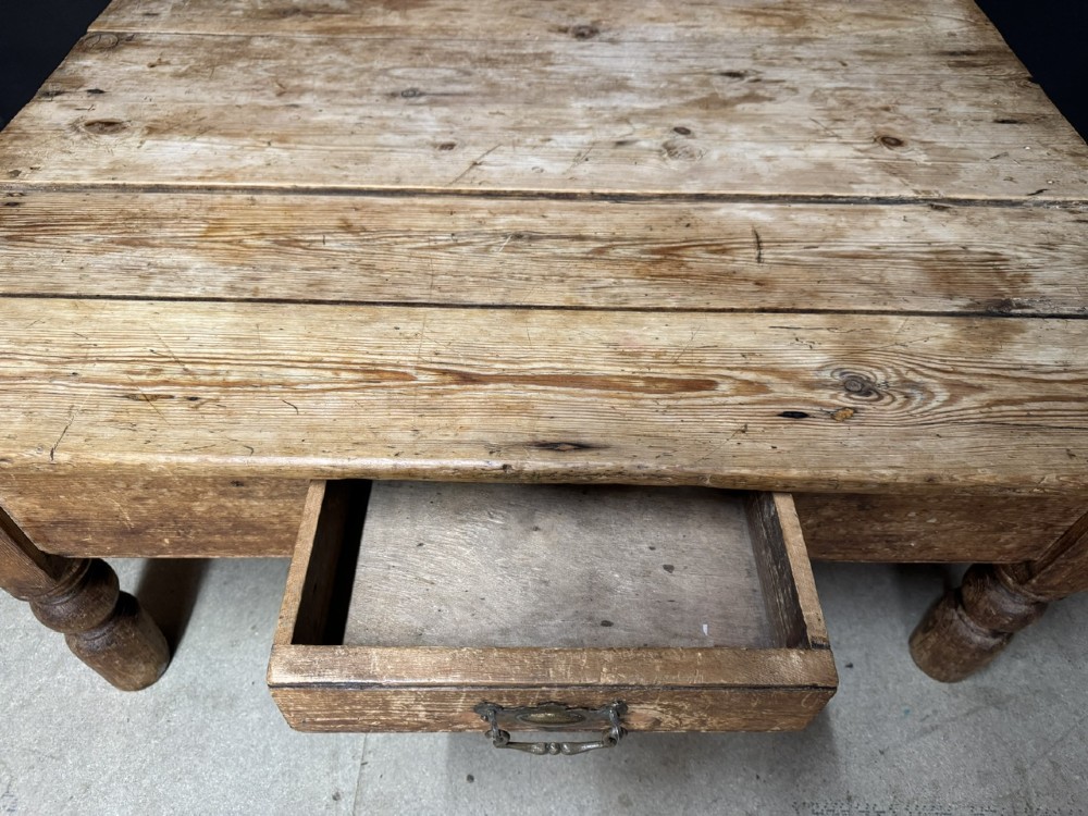 A low rectangular rustic pine coffee table featuring a plank top, turned corner legs, and a single central drawer with a brass drop handle. View V