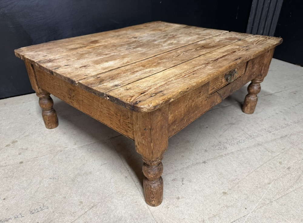 A low rectangular rustic pine coffee table featuring a plank top, turned corner legs, and a single central drawer with a brass drop handle. View VI