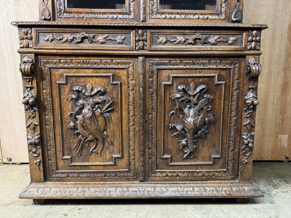A two-tier dark oak cabinet featuring arched glazed top doors, carved scroll motifs, and lower doors with relief carvings of game birds. View II