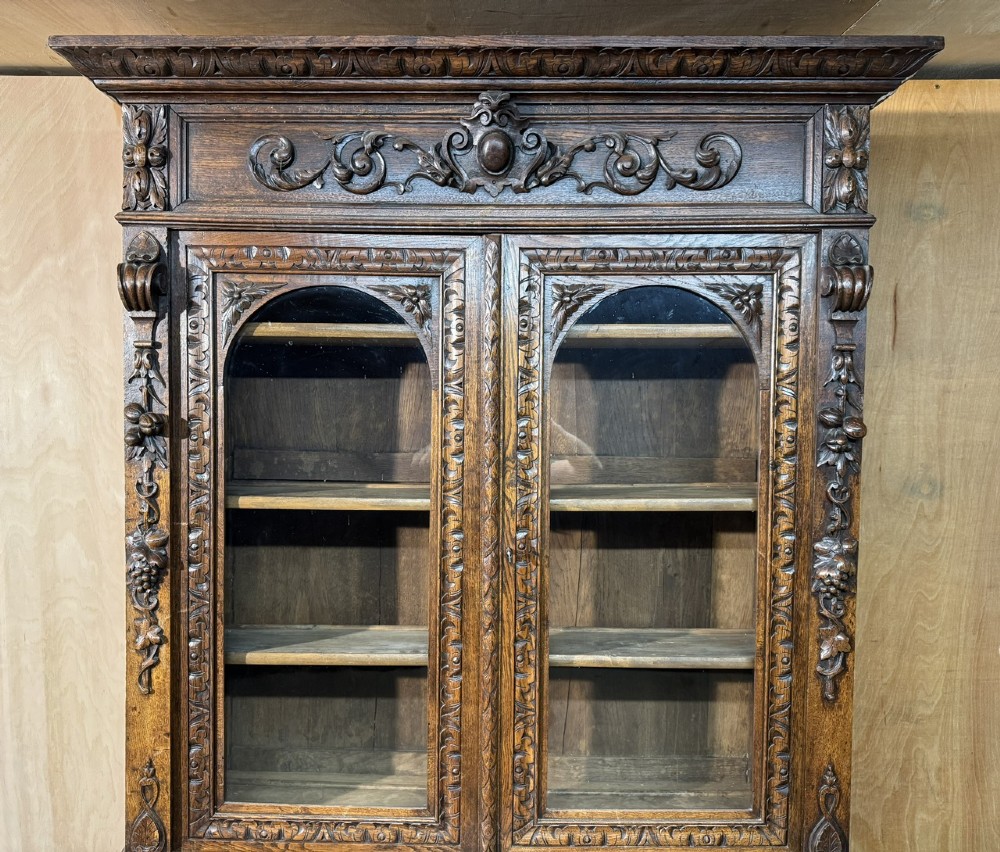 A two-tier dark oak cabinet featuring arched glazed top doors, carved scroll motifs, and lower doors with relief carvings of game birds. View III