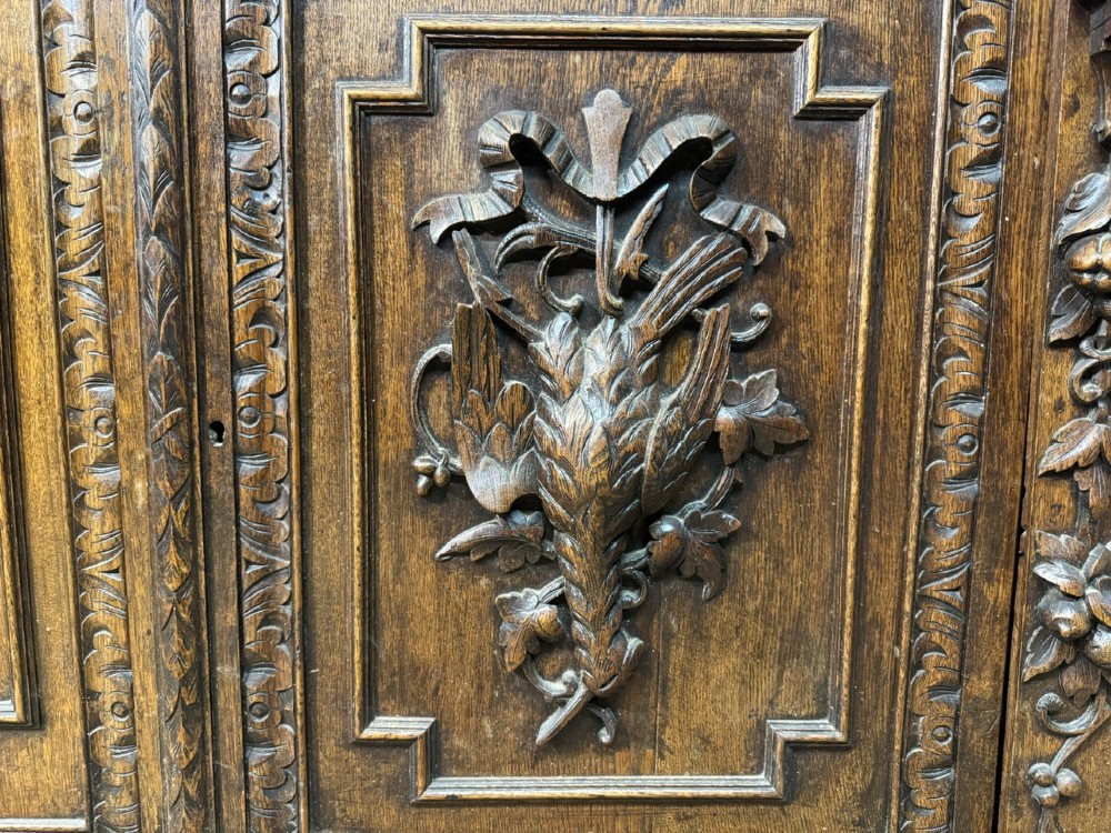 A two-tier dark oak cabinet featuring arched glazed top doors, carved scroll motifs, and lower doors with relief carvings of game birds. View IV