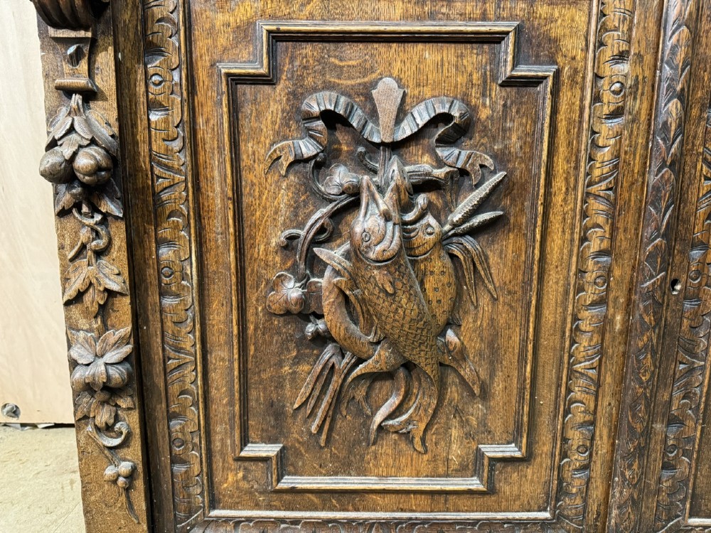 A two-tier dark oak cabinet featuring arched glazed top doors, carved scroll motifs, and lower doors with relief carvings of game birds. View V