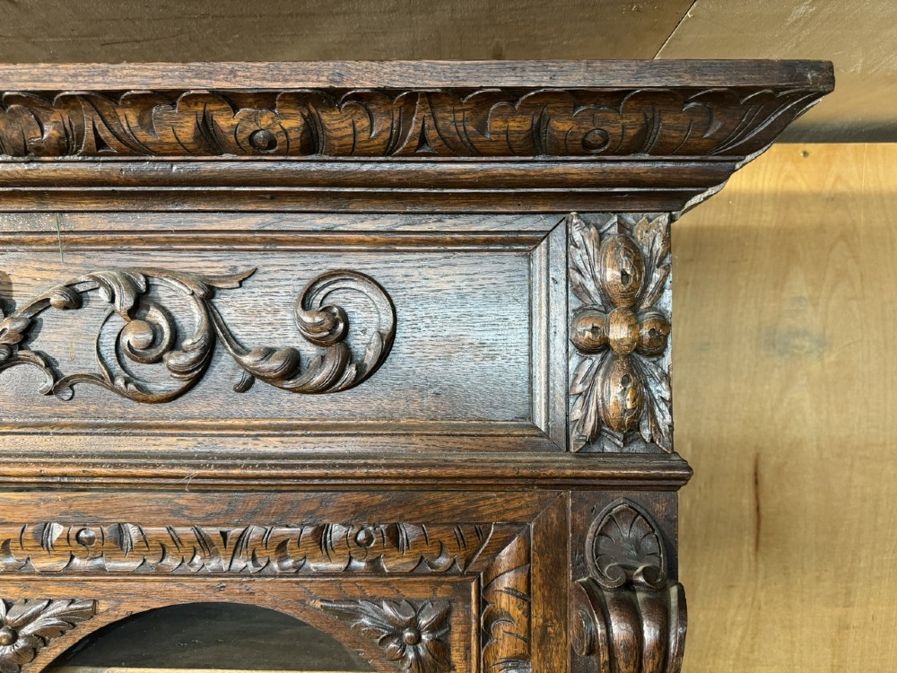 A two-tier dark oak cabinet featuring arched glazed top doors, carved scroll motifs, and lower doors with relief carvings of game birds. View XIII