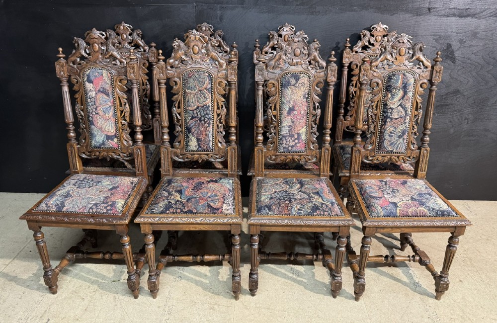 A set of eight high-backed dark oak dining chairs featuring carved lion crests and tapestry fabric upholstery.