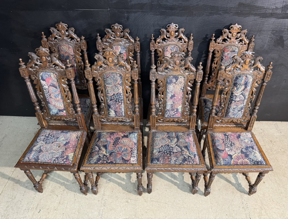 A set of eight high-backed dark oak dining chairs featuring carved lion crests and tapestry fabric upholstery. View IV